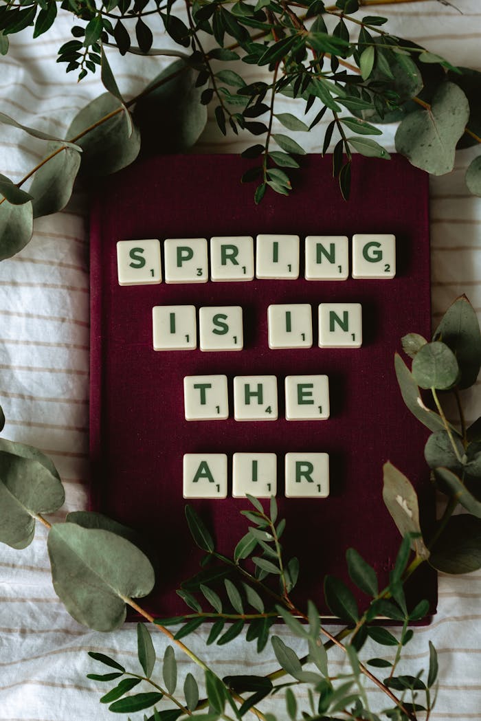Scrabble tiles on a purple background with eucalyptus spell Spring is in the Air. Perfect for seasonal themes.